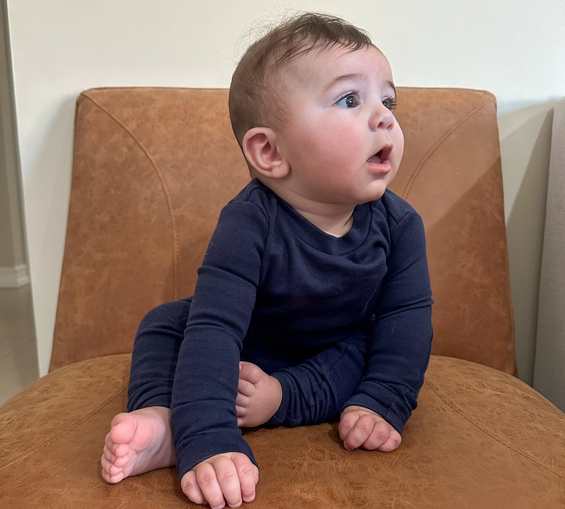 Baby sitting on a brown chair wearing a navy blue set